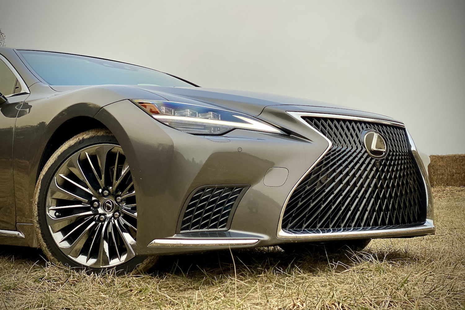 A close-up of the 2021 Lexus LS500's front end from passenger's side on a grassy field.