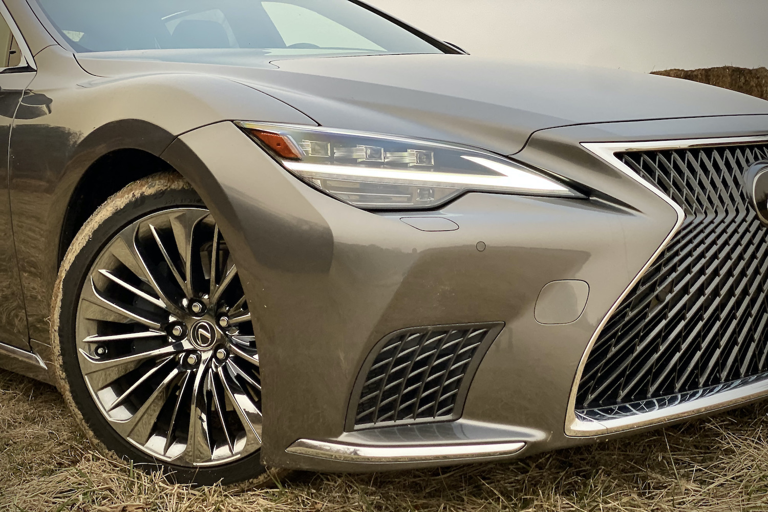 A close-up of the 2021 Lexus LS500's front headlight from passenger's side on a grassy field.
