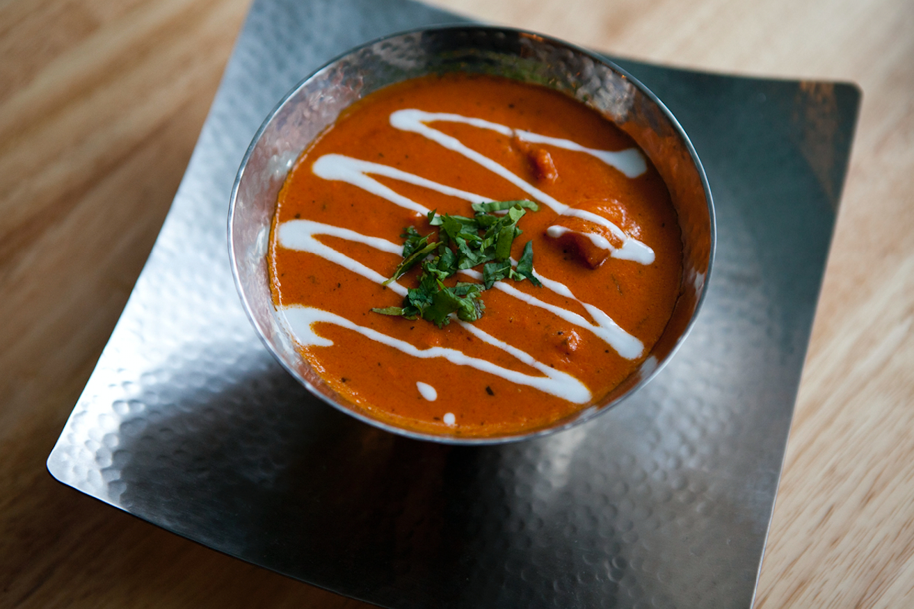 Moti Mahal Delux restaurant butter chicken topped with cream and chopped cilantro in a metal bowl on a metal plate. 