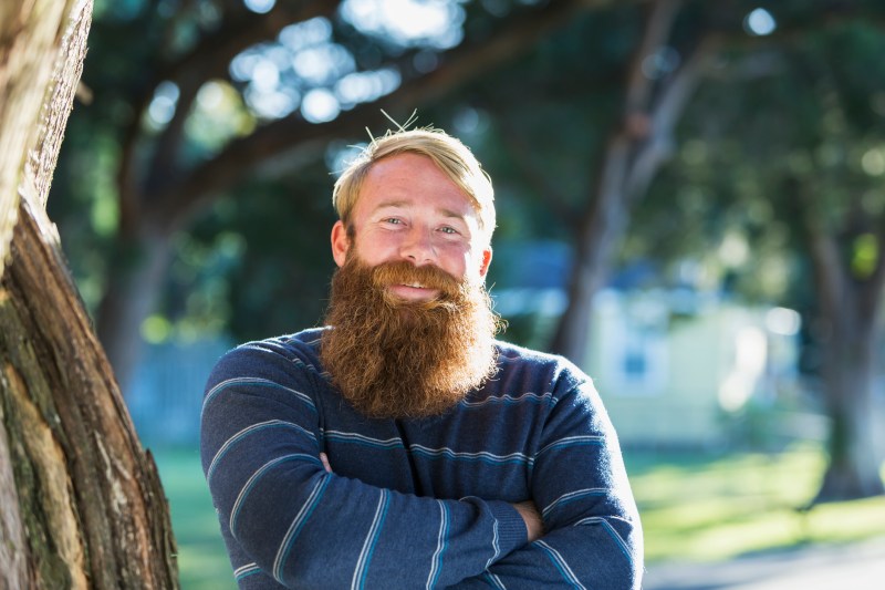 Man with blond hair and a long red beard, standing outdoors on a sunny day.