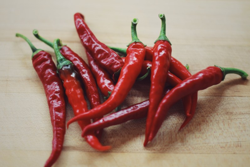 Handful of fresh red chilli peppers on a wooden table.