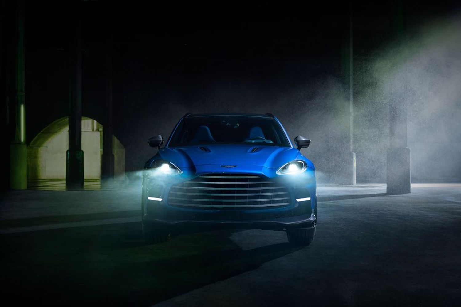 Aston Martin DBX 707 front end with headlights on in a dark warehouse.