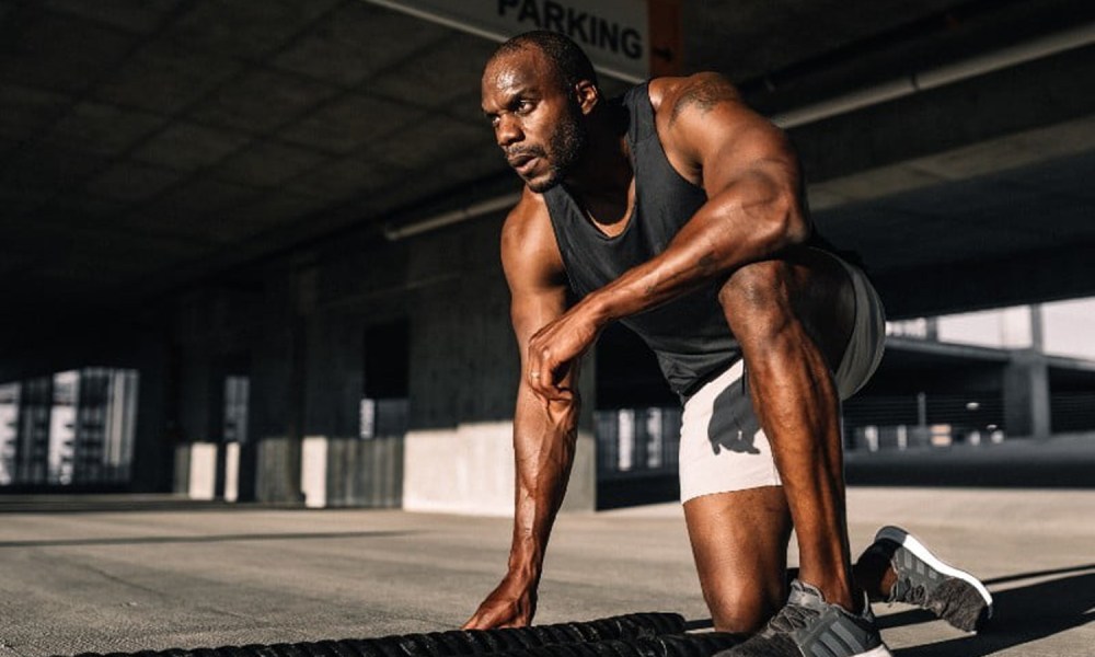 A man bending down on one knee in the middle of a workout.