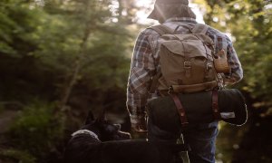 Man and dog walking in the woods with a wool blanket for camping strapped to a backpack