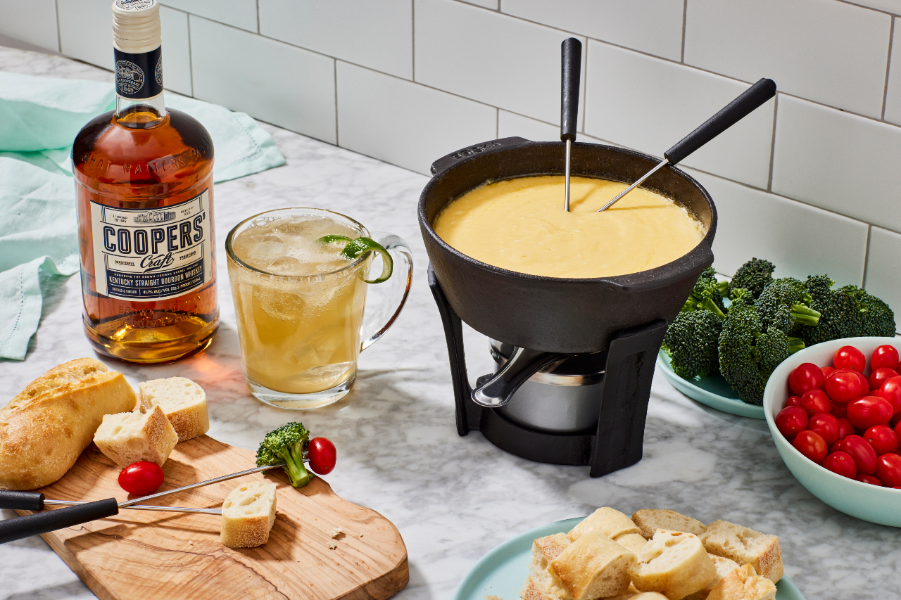 Bourbon fondue with bottle of Coopers' and bread cubes, veggies on a marble surface.