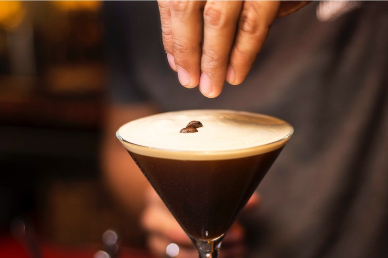 Person holding an espresso martini glass placing coffee beans as a garnish.