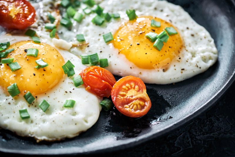 Sunny-side-up eggs with tomatoes and greens on a plate. 