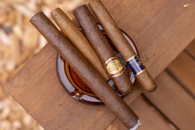 Selection of cigars in an ashtray resting on a wooden table.