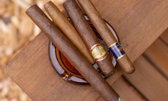 Selection of cigars in an ashtray resting on a wooden table.