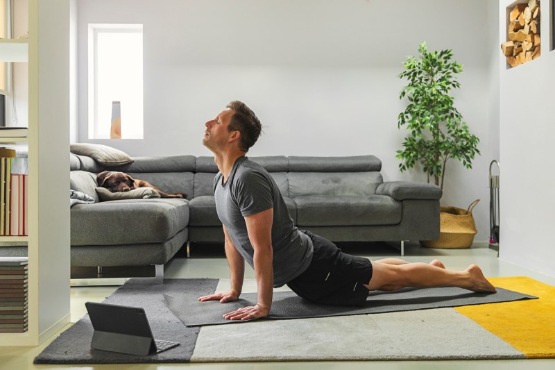 A man doing a yoga pose with a tablet in front of him in the living room.