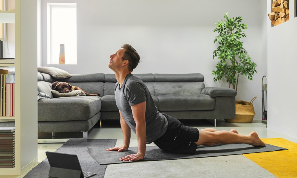 A man doing a yoga pose with a tablet in front of him in the living room.