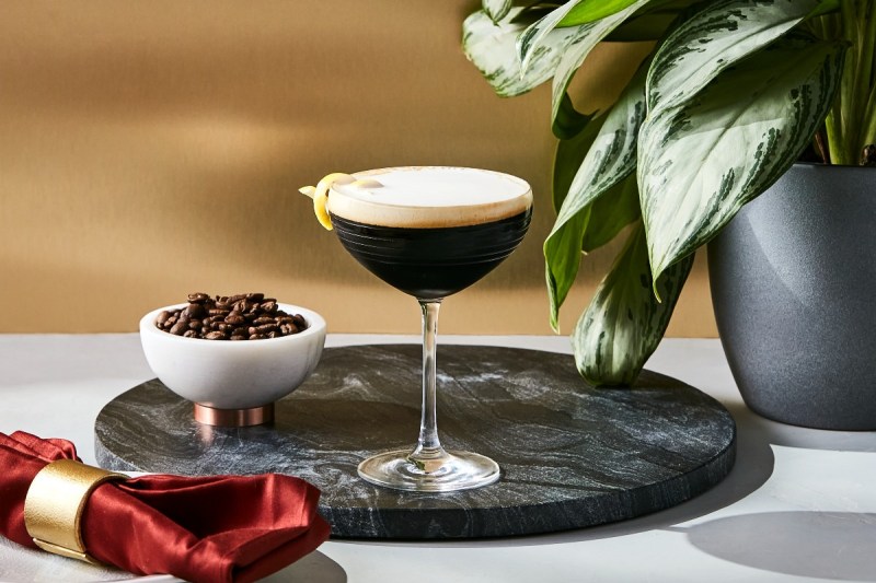 Ketel One espresso martini sitting on a tray next to coffee beans in a dish.