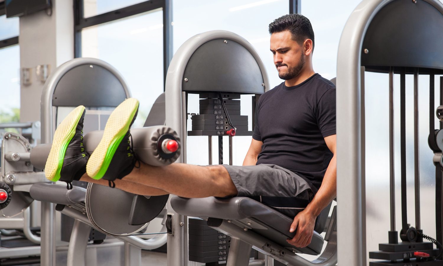 A male athlete doing leg extensions on a machine in a gym.