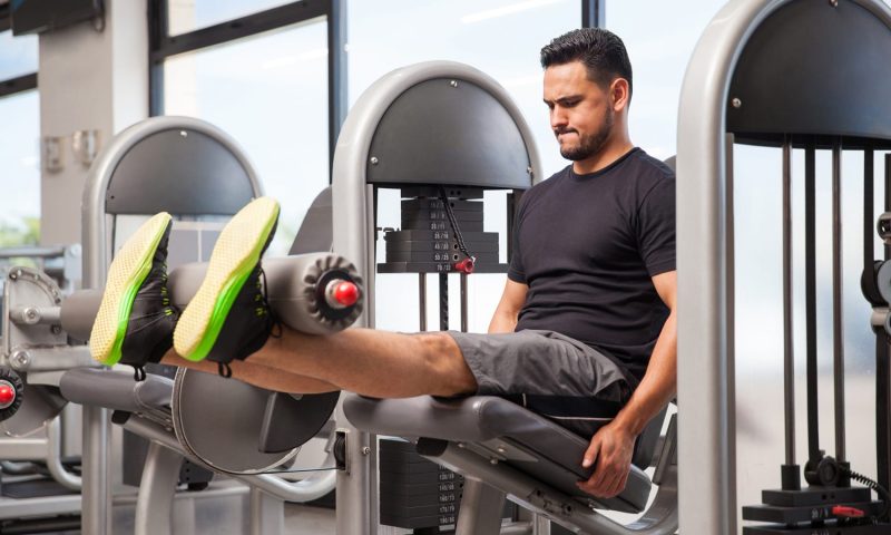 A male athlete doing leg extensions on a machine in a gym.
