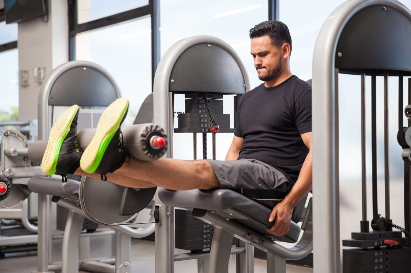 A male athlete doing leg extensions on a machine in a gym.