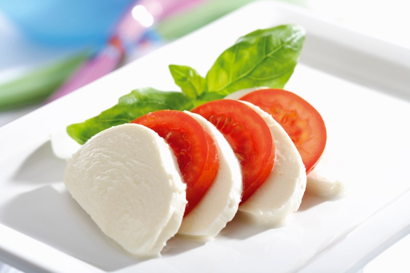 Mozzarella cheese slices with tomatoes and herbs on a plate.