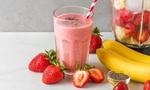 A glass of strawberry smoothie, surrounded by strawberries and bananas.