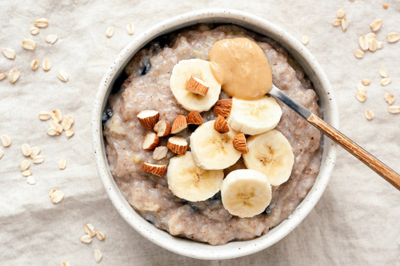 A spoonful of peanut butter and a bowl of oatmeal with banana slices.
