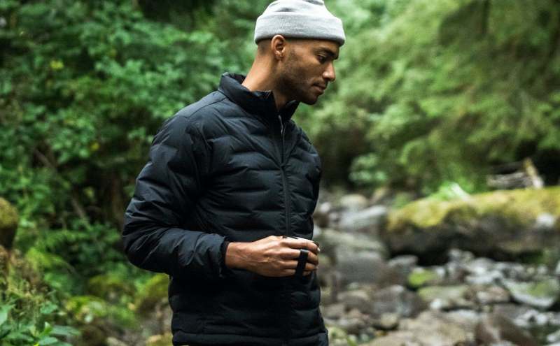 Man in the woods wearing Proof and holding a cup.