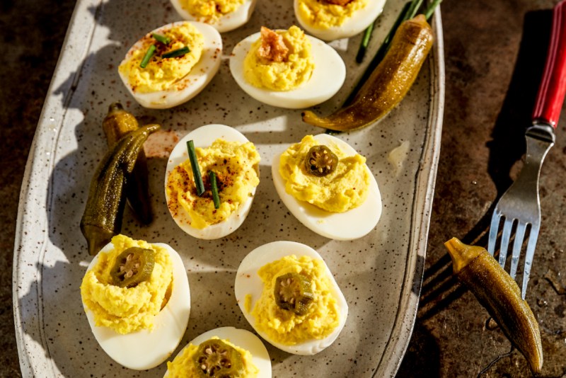 Rodney Scott deviled eggs with pickled okra on a metal tray with a red fork.