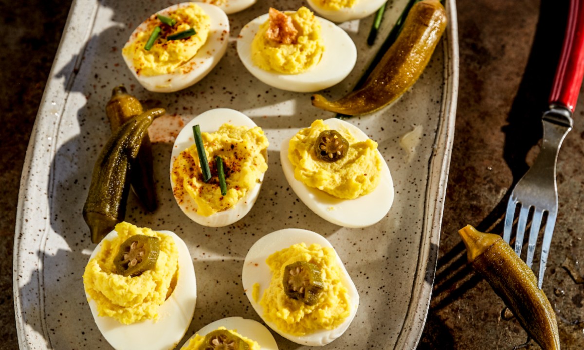 Rodney Scott deviled eggs with pickled okra on a metal tray with a red fork.