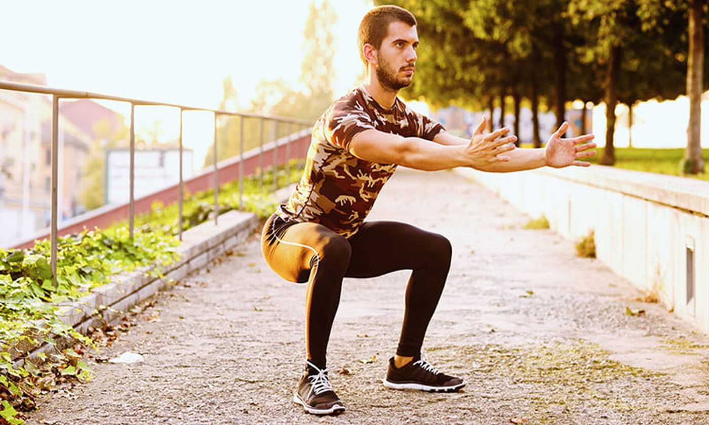 A man doing sumo squats in a park.