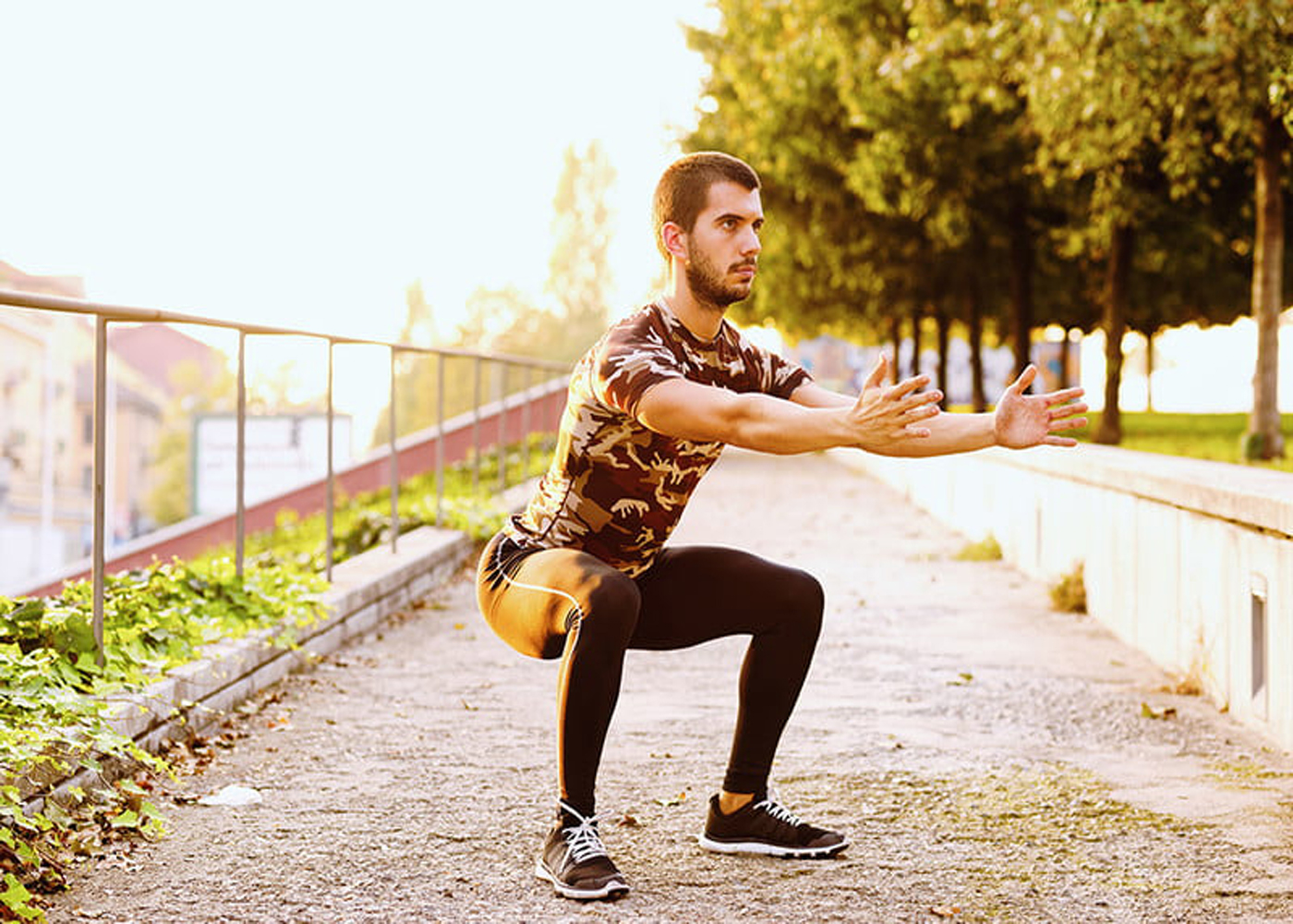 A man doing sumo squats in a park.