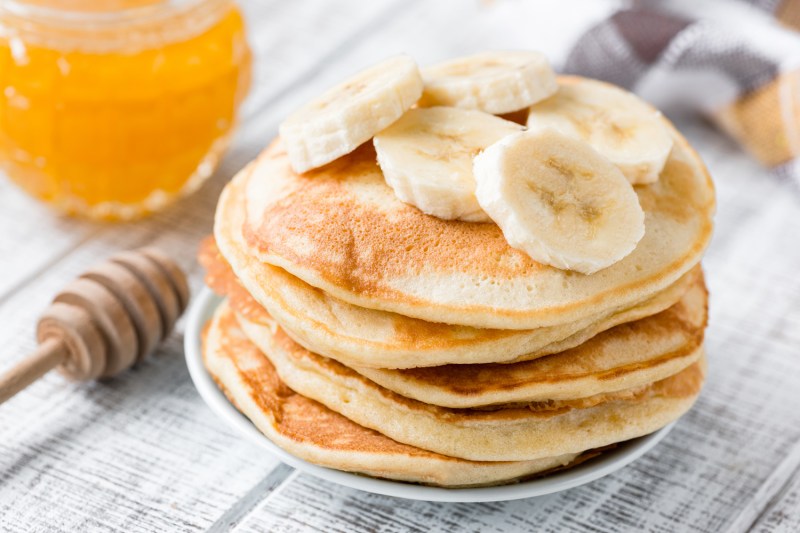Plastry banana na talerzu naleśników obok filiżanki miodu na stole.