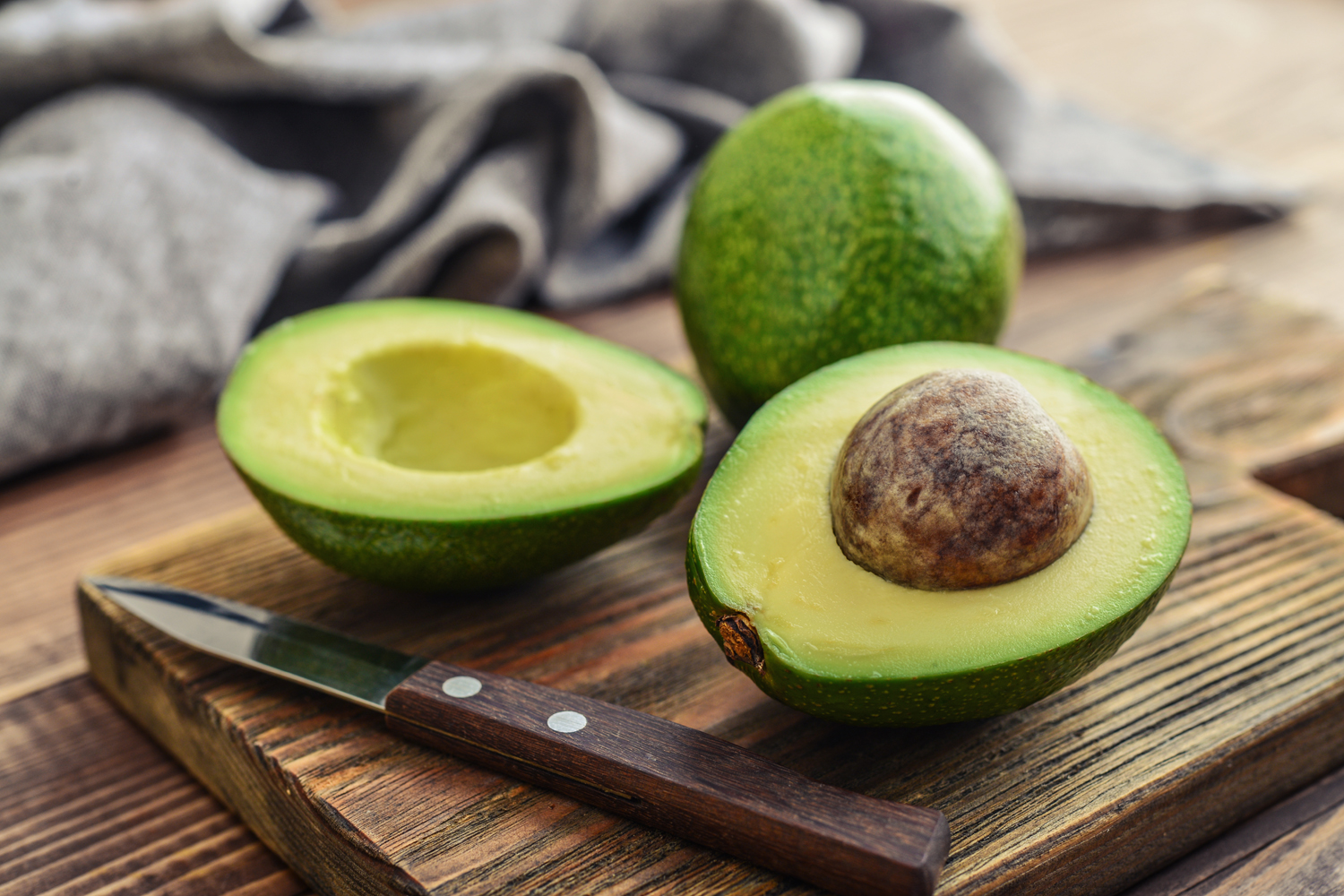 A sliced avocado and whole avocado with knife on a wooden cutting board