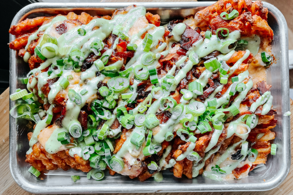 A tray of Emmy Squared waffles fries covered in toppings on a metal tray.