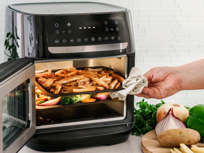 12.6-quart Bella Pro Series digital air fryer oven being opened with french fries on the top shelf and vegetables on the bottom.