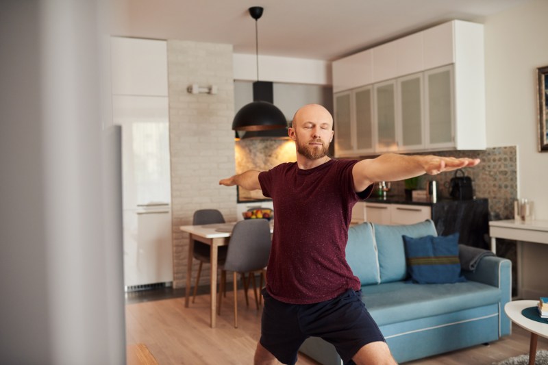A man doing a closed eyes warrior pose in the living room.