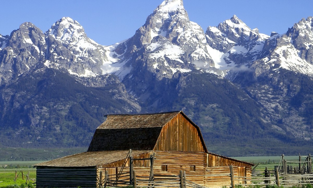 A rustic wood barn sits beneath a panorama of the Grand Teton Mountains in Jackson Hole, Wyoming