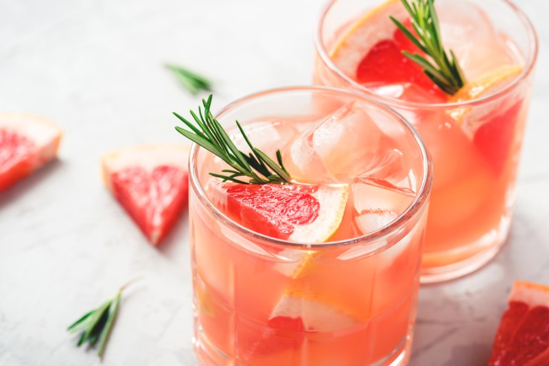 Two glasses of grapefruit cocktail with grapefruit slices and rosemary garnish on a table.