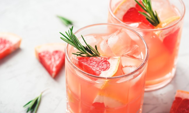 Two glasses of grapefruit cocktail with grapefruit slices and rosemary garnish on a table