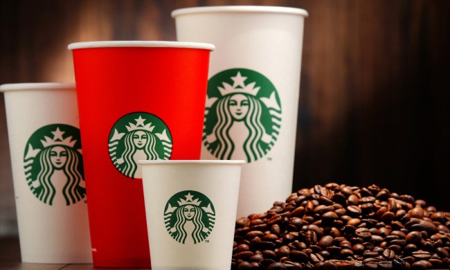 A red Starbucks cup in between three white Starbucks cups beside coffee beans.