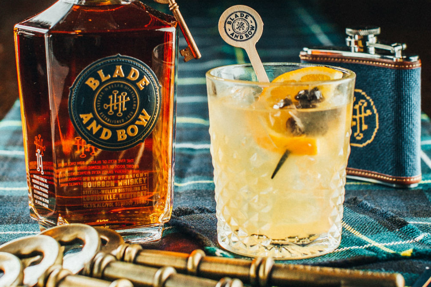 A glass of Blade and Bow New Fashioned cocktail with orange and blueberry skewer garnish beside a bottle of Kentucky Straight Bourbon Whiskey.
