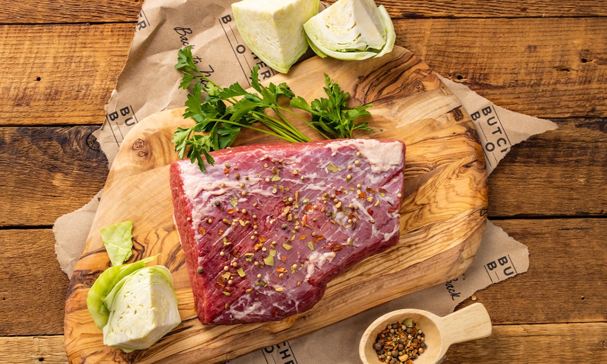 ButcherBox corned beef brisket with aromatics on wooden board.
