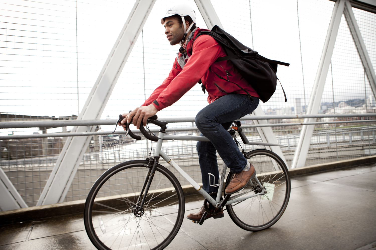 A man with black backpack and white helmet cycling to work on a road.