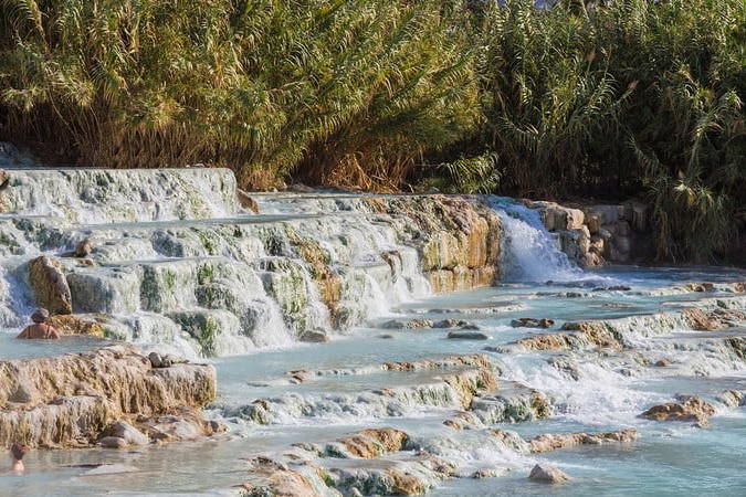 A blue hot springs area, surrounded by greenery and rocks within the waters.