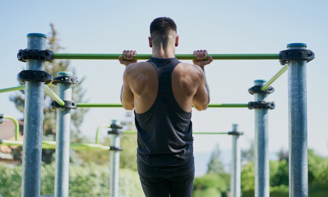 A man in black sleeveless top doing pull ups with a bar at a park.