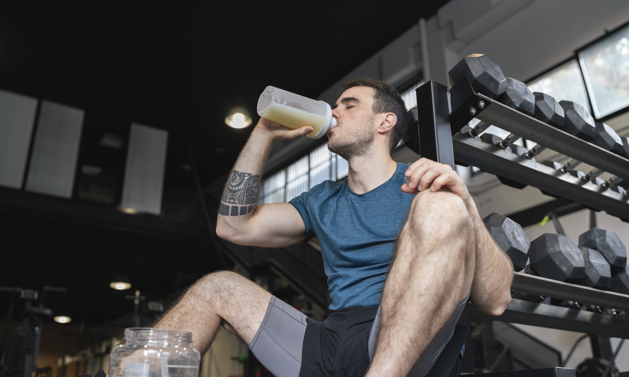 Male athlete drinking protein shake while sitting in gym.