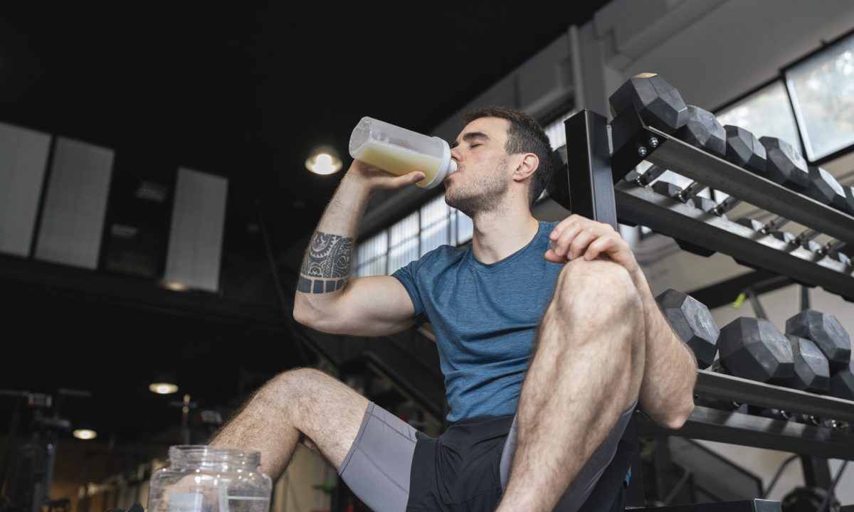 Male athlete drinking protein shake while sitting in gym