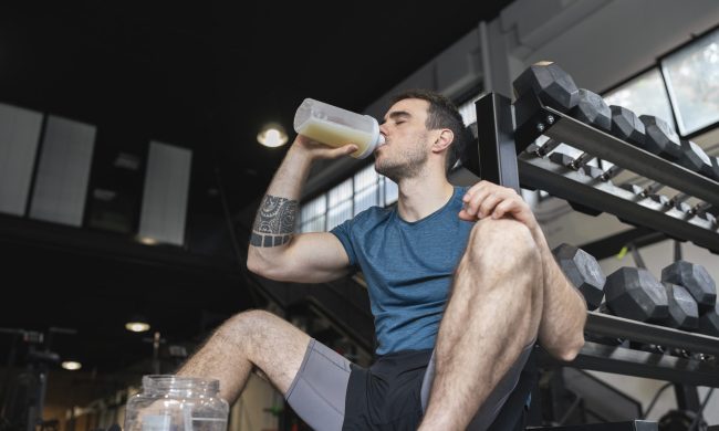 Male athlete drinking protein shake while sitting in gym