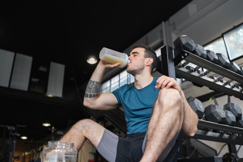 Male athlete drinking protein shake while sitting in gym.