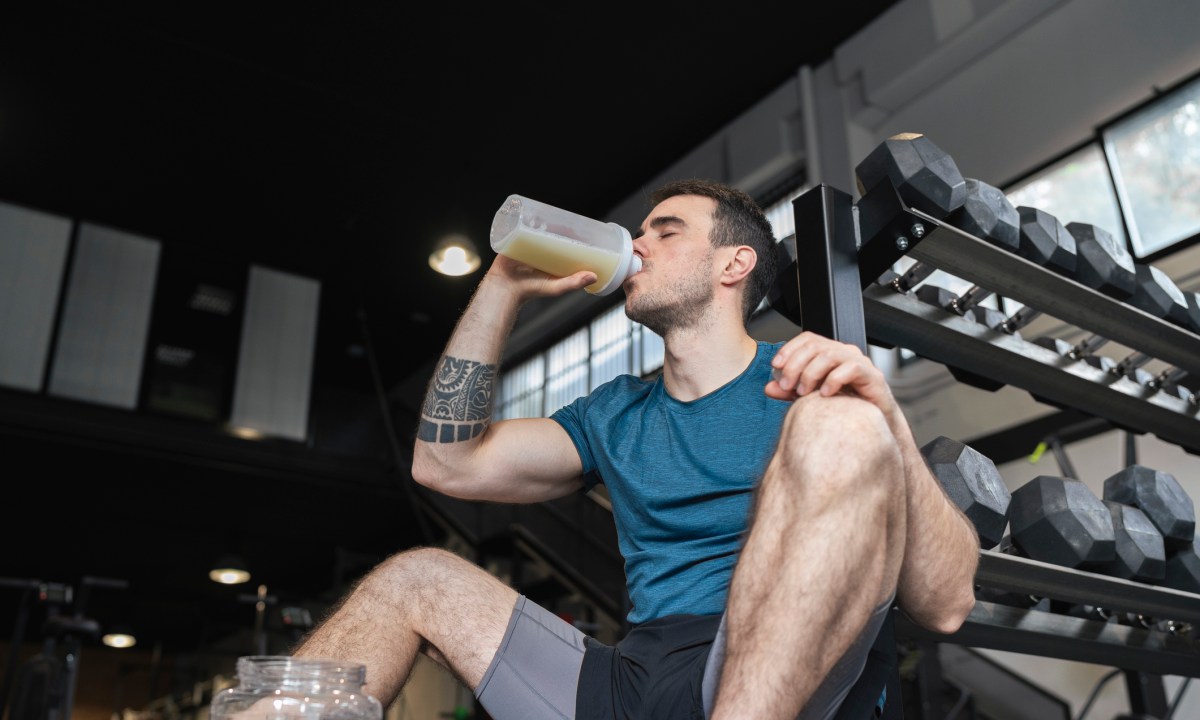 Male athlete drinking protein shake while sitting in gym