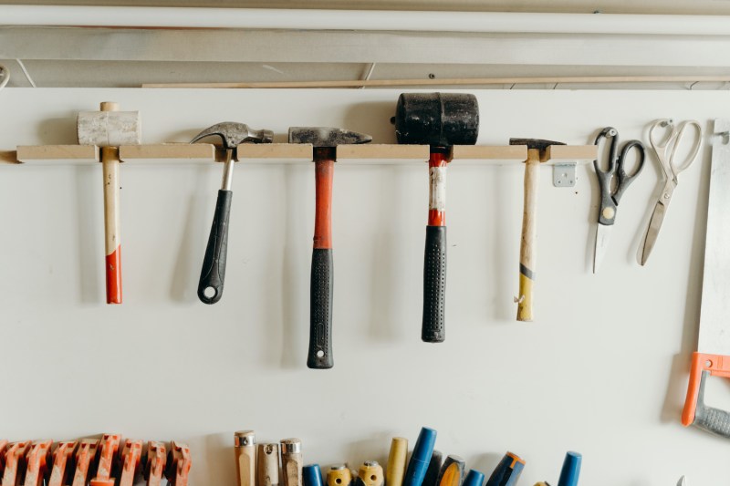 Tools hanging on white wall by a thin piece of wood.