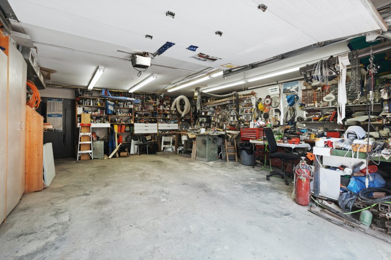 A cluttered garage with tools on shelves and a dirty floor.