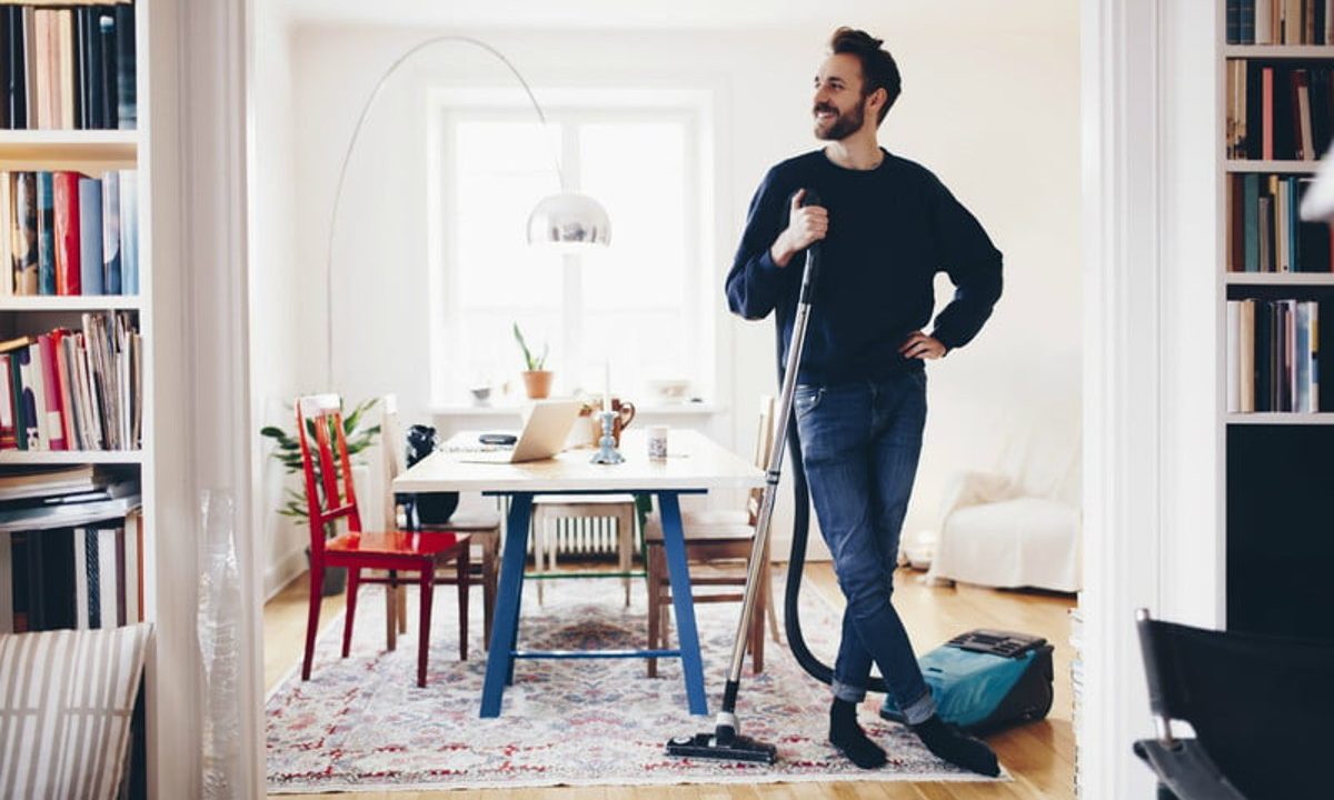 Man smiling in clean apartment holding a vacuum.