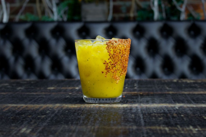 An ice-cold glass of Mango Basil Margarita on black table.